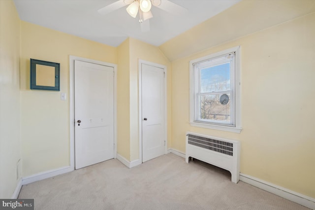 unfurnished bedroom featuring vaulted ceiling, light carpet, radiator, ceiling fan, and a baseboard heating unit