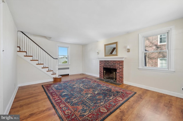 living room featuring wood-type flooring, a brick fireplace, and a baseboard heating unit