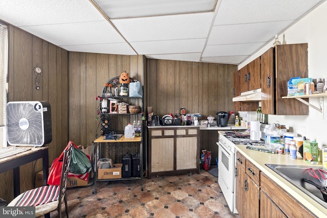 kitchen with a paneled ceiling, wooden walls, and gas range gas stove