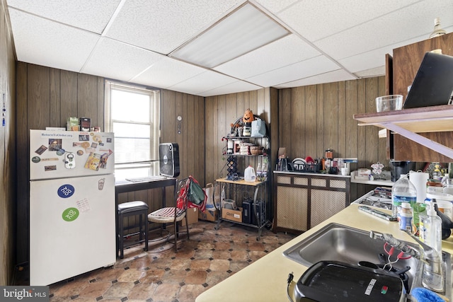 kitchen featuring sink, a paneled ceiling, wooden walls, and white refrigerator