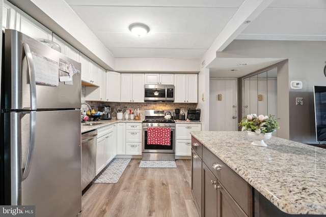 kitchen featuring stainless steel appliances, white cabinetry, light stone counters, and light hardwood / wood-style flooring