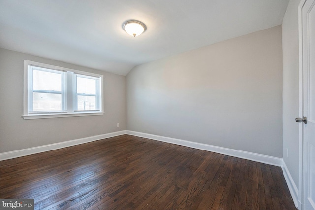 spare room with dark wood-type flooring, vaulted ceiling, and baseboards