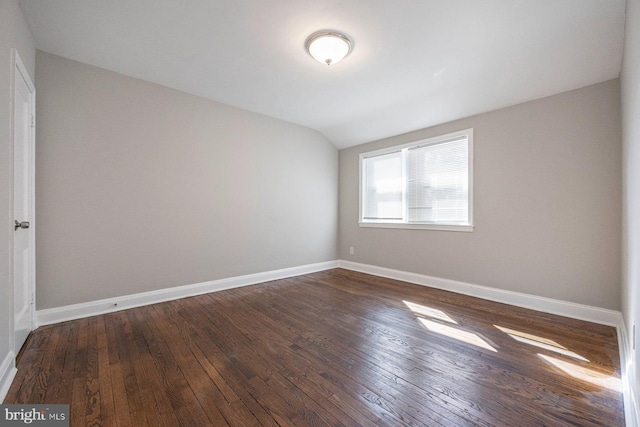 spare room with dark wood-style floors, vaulted ceiling, and baseboards