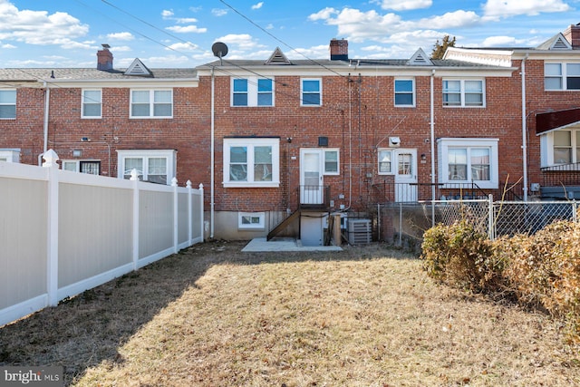 back of house featuring central AC unit, a fenced backyard, a chimney, a yard, and brick siding