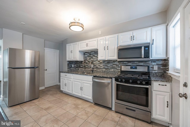 kitchen with dark stone counters, appliances with stainless steel finishes, a sink, and white cabinetry