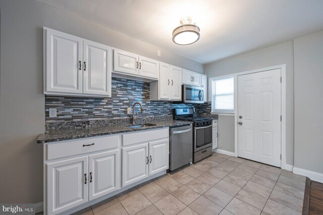 kitchen featuring tasteful backsplash, white cabinets, dark stone counters, appliances with stainless steel finishes, and a sink