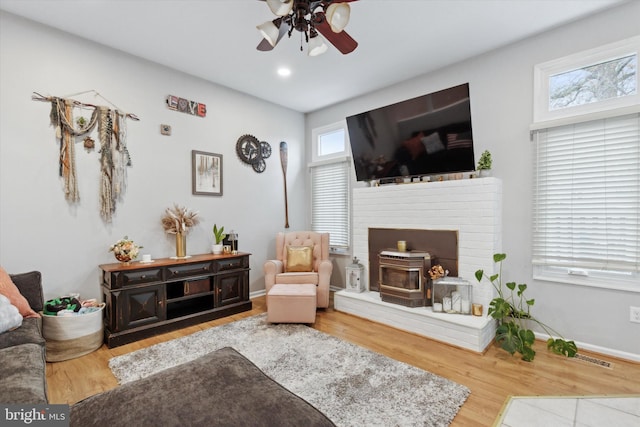 living area featuring recessed lighting, a ceiling fan, a wood stove, wood finished floors, and baseboards