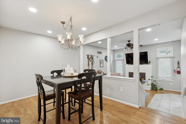 dining space featuring recessed lighting, ceiling fan with notable chandelier, baseboards, light wood-type flooring, and a brick fireplace