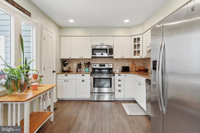 kitchen with butcher block counters, white cabinets, appliances with stainless steel finishes, backsplash, and glass insert cabinets