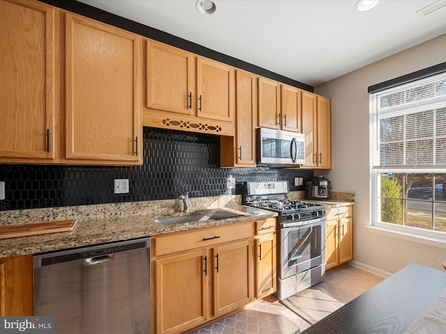 kitchen with light tile patterned flooring, sink, light stone counters, stainless steel appliances, and backsplash