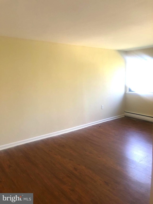 spare room with a baseboard heating unit and dark hardwood / wood-style floors