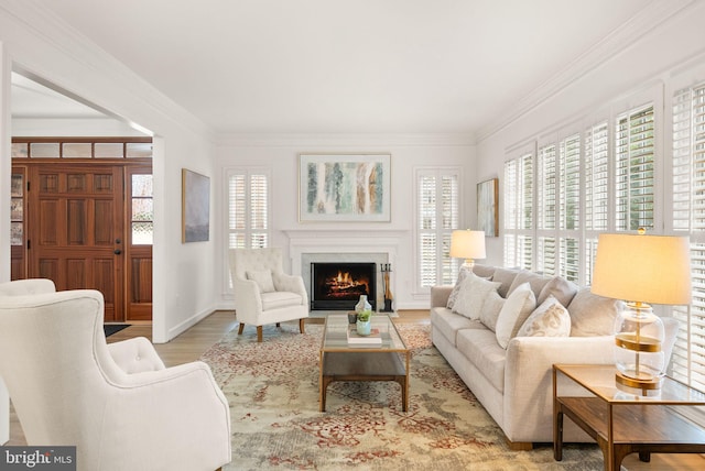 living area with a lit fireplace, crown molding, light wood-style flooring, and baseboards