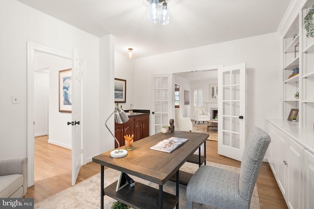 office area with light wood-style floors, baseboards, a sink, and french doors