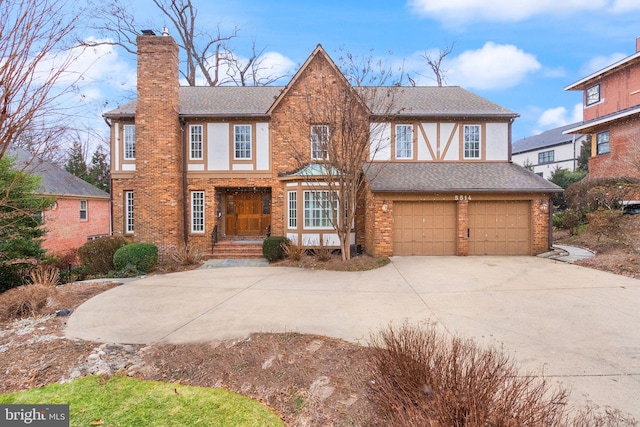 tudor house with driveway, a garage, a chimney, and brick siding