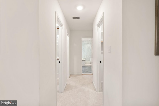 hallway featuring baseboards, visible vents, and light colored carpet