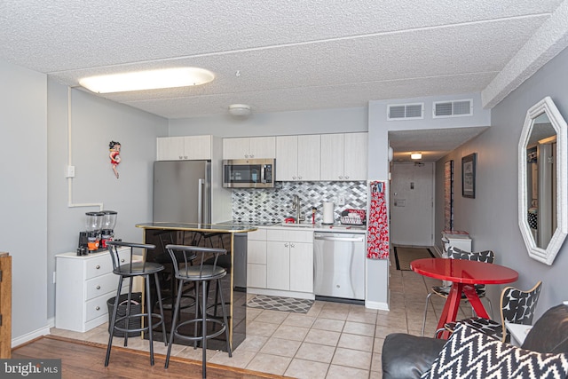 kitchen featuring light tile patterned floors, appliances with stainless steel finishes, backsplash, a textured ceiling, and white cabinets