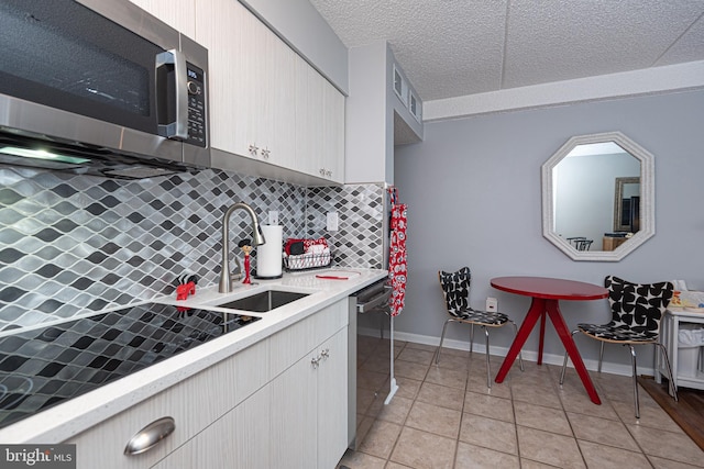 kitchen featuring sink, light tile patterned floors, backsplash, stainless steel appliances, and a textured ceiling