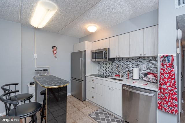 kitchen featuring light tile patterned flooring, sink, backsplash, stainless steel appliances, and a textured ceiling