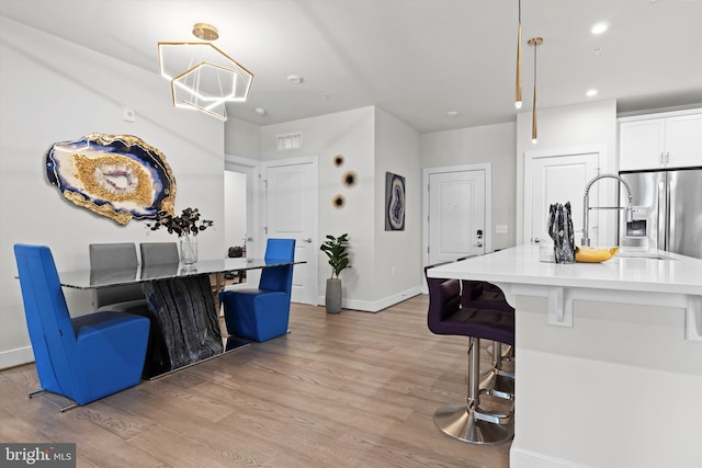 kitchen with a kitchen bar, stainless steel fridge, pendant lighting, light hardwood / wood-style floors, and white cabinets