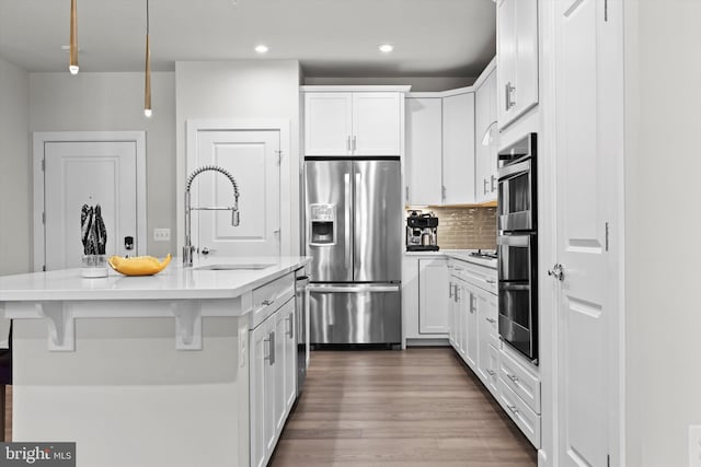 kitchen featuring sink, white cabinetry, stainless steel appliances, a center island with sink, and decorative backsplash