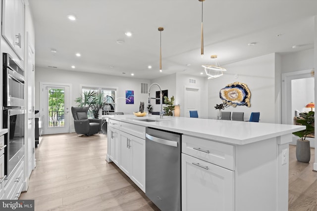 kitchen featuring light hardwood / wood-style flooring, white cabinetry, a kitchen island with sink, stainless steel appliances, and decorative light fixtures