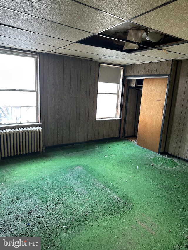 unfurnished bedroom featuring carpet flooring, wooden walls, and radiator