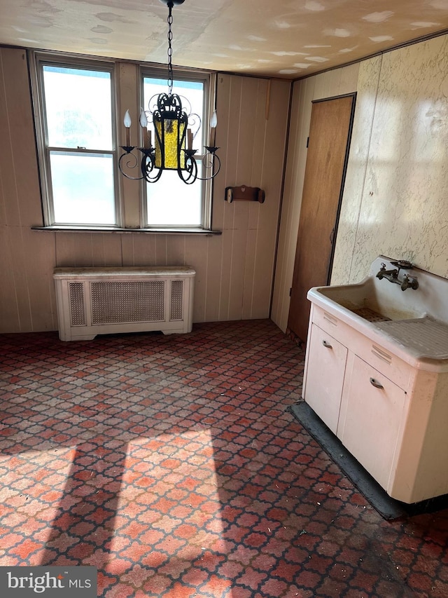 unfurnished dining area featuring radiator, sink, a notable chandelier, and wood walls