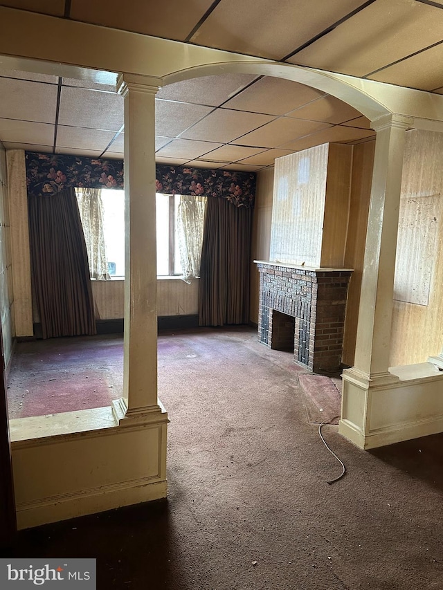 unfurnished living room with decorative columns, carpet flooring, and a drop ceiling