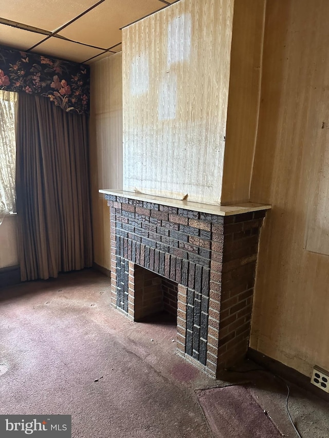 unfurnished living room featuring a paneled ceiling, carpet floors, and a brick fireplace