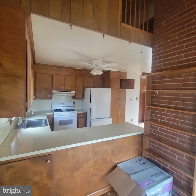 kitchen featuring white appliances, brown cabinetry, a peninsula, light countertops, and a sink