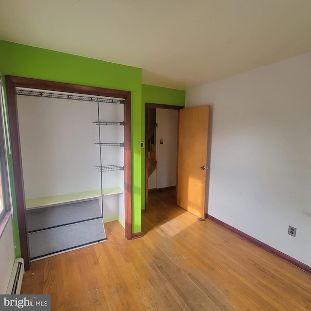 unfurnished bedroom featuring light wood finished floors, baseboards, baseboard heating, and a closet