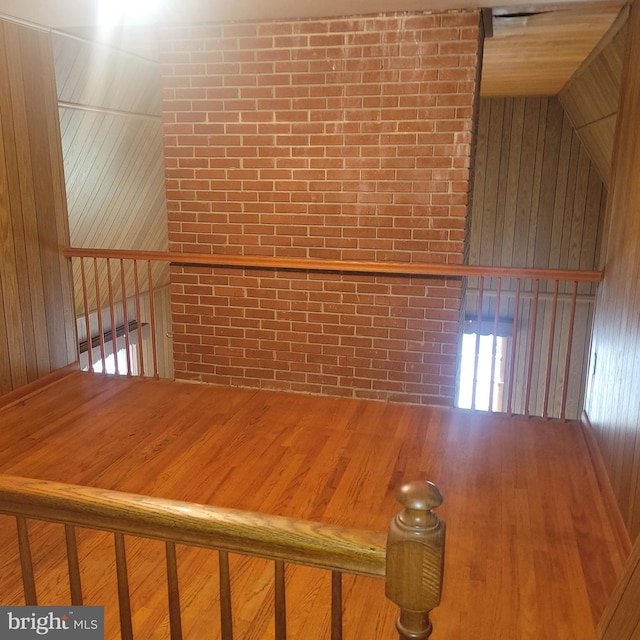 spare room with lofted ceiling, brick wall, wood finished floors, and wooden walls