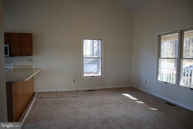 interior space with high vaulted ceiling, electric range, light colored carpet, and a healthy amount of sunlight