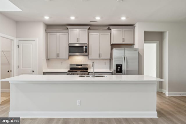 kitchen with appliances with stainless steel finishes, sink, a center island with sink, and gray cabinetry