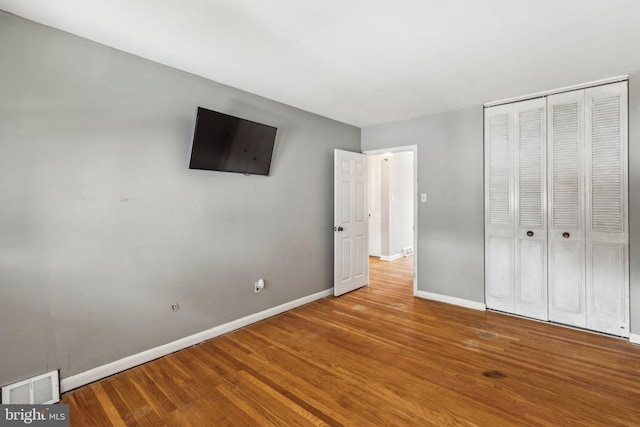 unfurnished bedroom featuring baseboards, visible vents, wood finished floors, and a closet