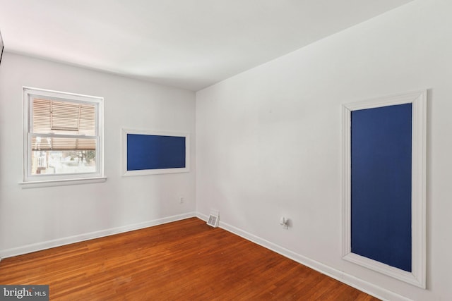 unfurnished room with baseboards, wood finished floors, and visible vents