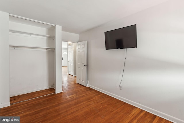 unfurnished bedroom featuring baseboards, wood finished floors, and a closet