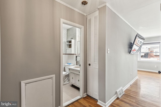 hall with light wood-style flooring, visible vents, baseboards, and crown molding