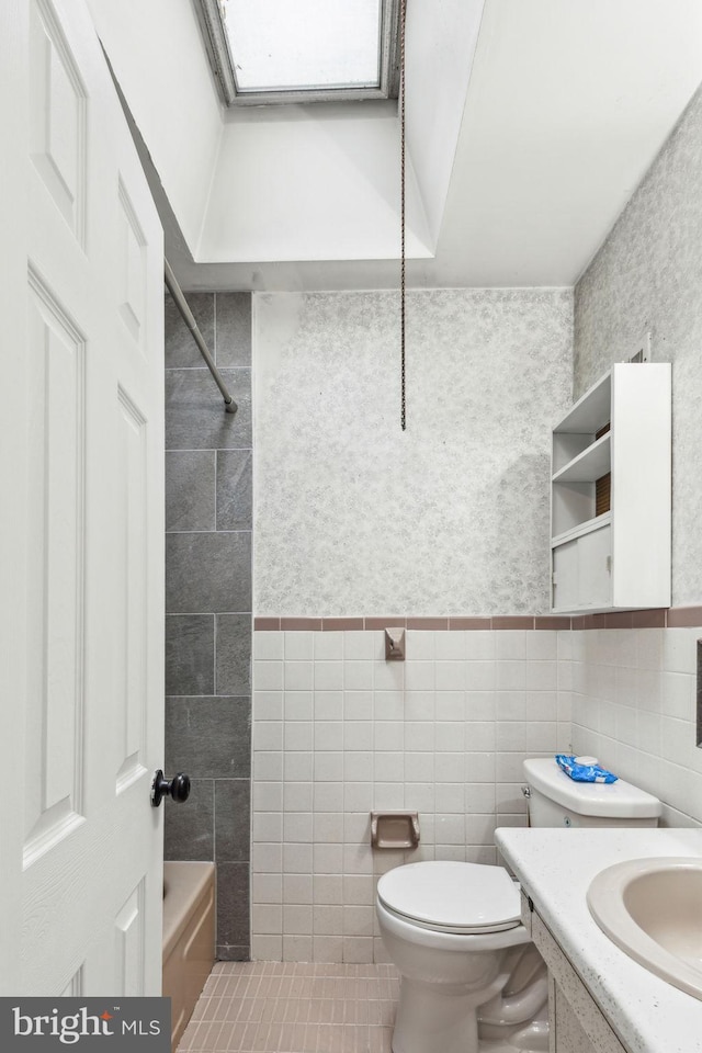 full bathroom with vanity, a skylight, wainscoting, and tile walls