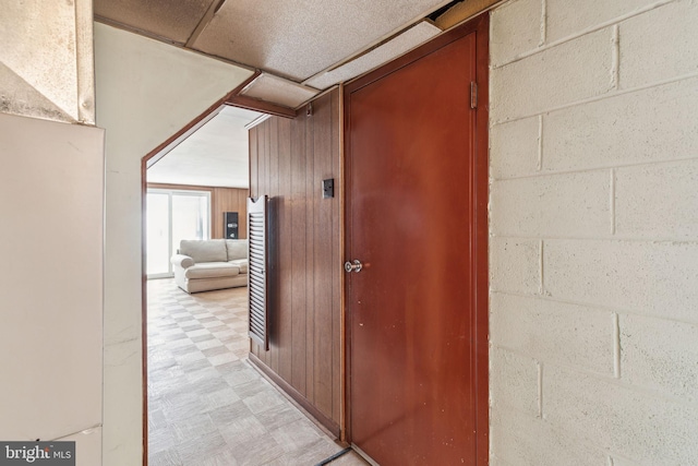 hall with light floors, concrete block wall, and wood walls