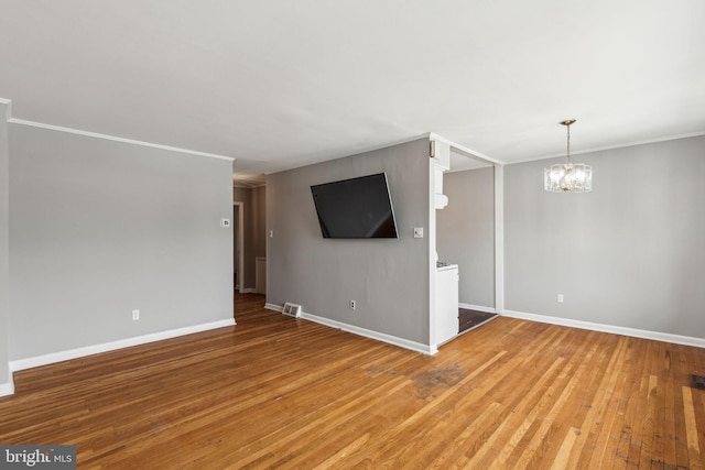 unfurnished living room with crown molding, wood finished floors, baseboards, an inviting chandelier, and visible vents