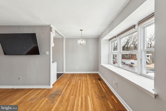 unfurnished dining area featuring baseboards, wood finished floors, and a notable chandelier