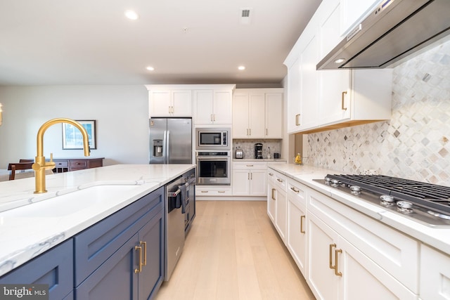 kitchen with blue cabinetry, extractor fan, stainless steel appliances, light stone countertops, and white cabinets