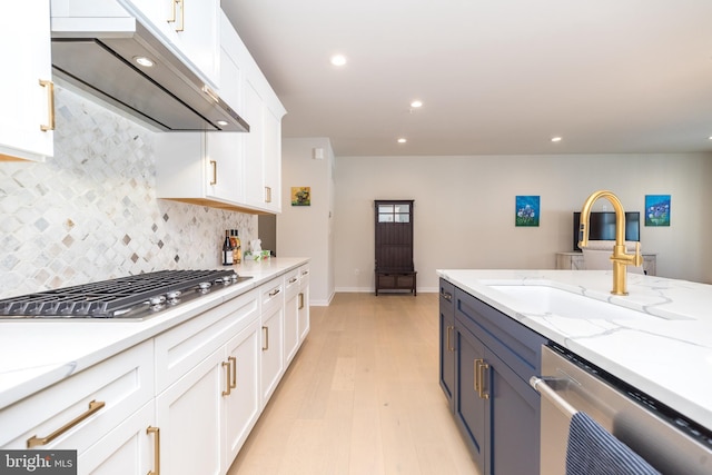 kitchen with sink, wall chimney range hood, stainless steel appliances, light stone countertops, and white cabinets