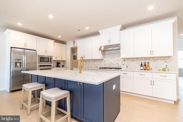 kitchen featuring white cabinetry, appliances with stainless steel finishes, a kitchen island with sink, and light stone counters