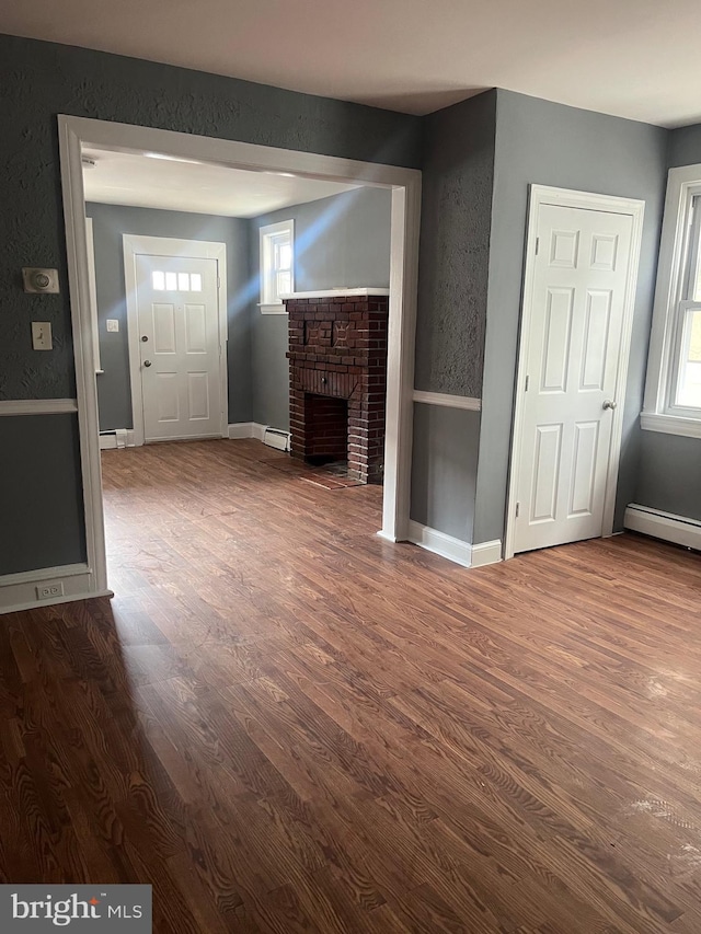 unfurnished living room featuring dark wood-type flooring, a fireplace, and a baseboard heating unit