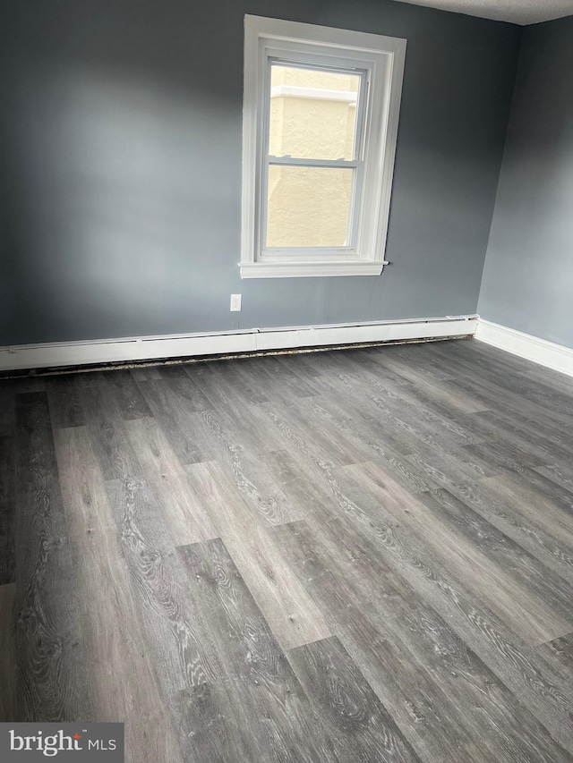 unfurnished room featuring hardwood / wood-style floors and a baseboard heating unit