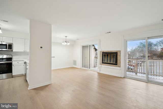 unfurnished living room featuring a notable chandelier and light wood-type flooring