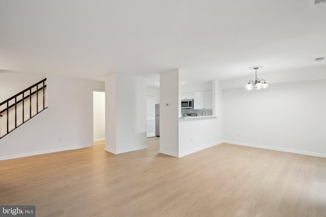 unfurnished living room featuring a chandelier and light hardwood / wood-style flooring