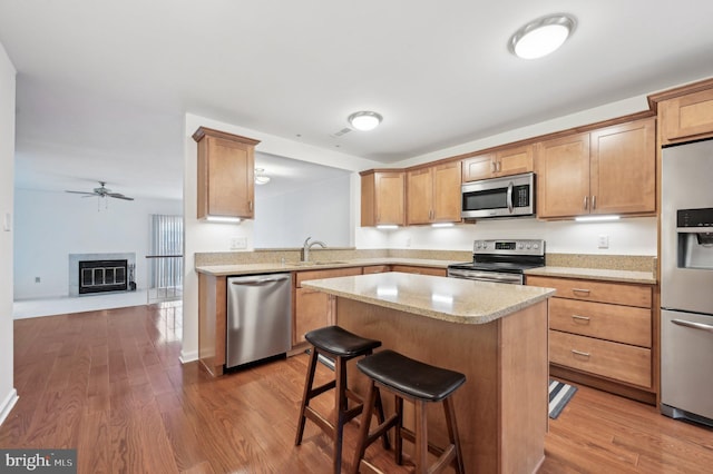 kitchen featuring a breakfast bar area, ceiling fan, hardwood / wood-style floors, stainless steel appliances, and a kitchen island